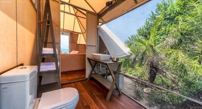 Kodev - wooden cabin interior with toilet, desk, and open railing overlooking trees