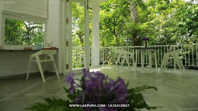 Ceylon Olive - covered porch with purple flowers, white chairs, forest view beyond railing