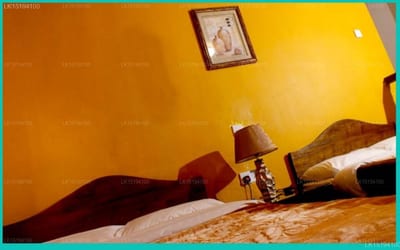Tinithi Villa - bright yellow bedroom wall with bed and framed portrait