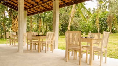 Ambarella Lodge - Katunayake - wooden dining tables and chairs under covered pavilion, tropical gardens beyond