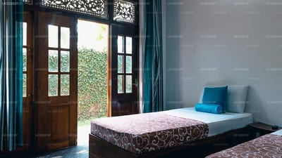 Hostel First - single bed with patterned mattress, wooden doors opening to garden