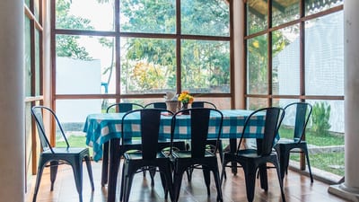 Hostel First - dining area with black chairs and blue checkered tablecloth by windows